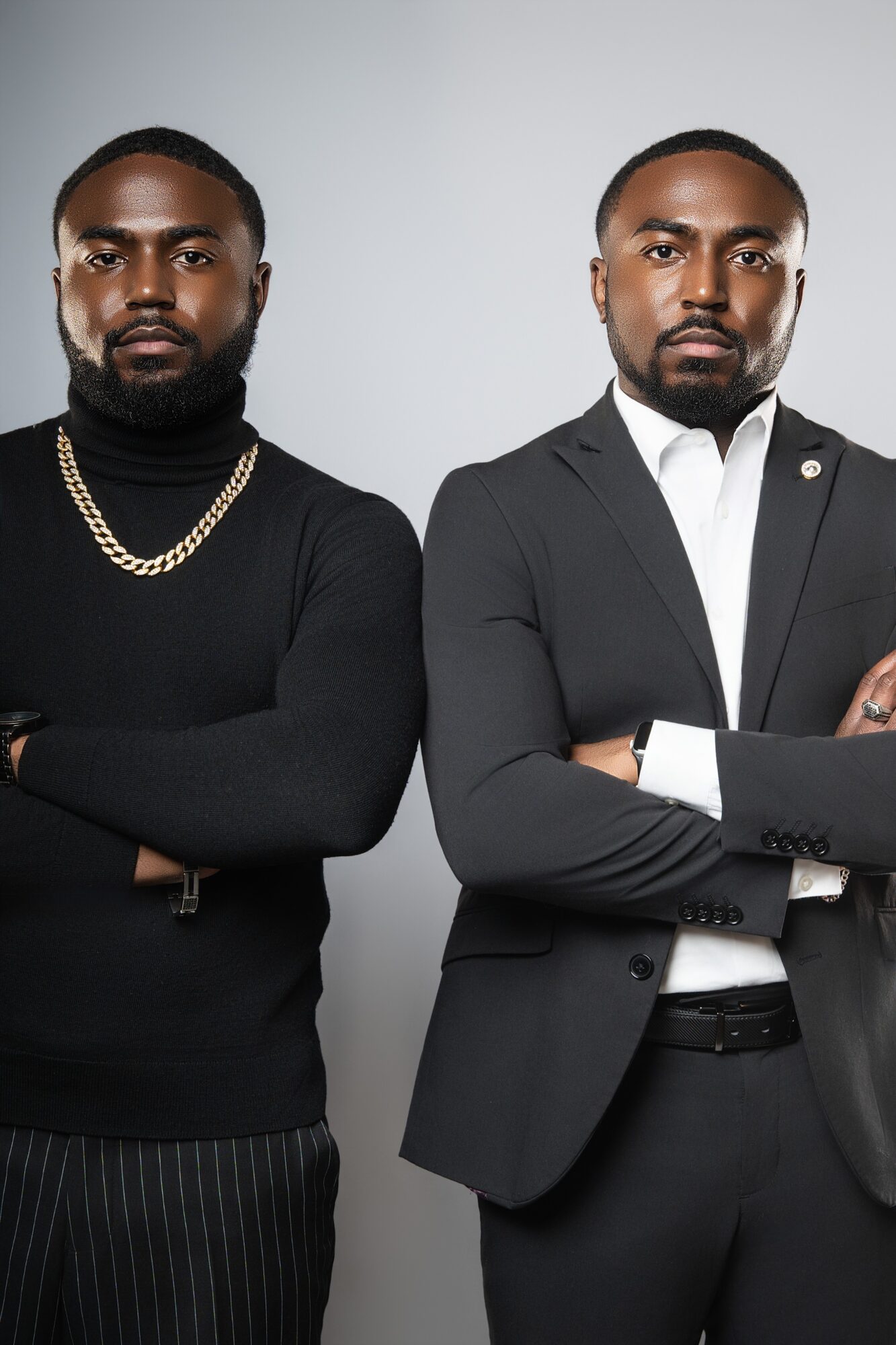 Two men stand side by side with arms crossed, dressed in formal and casual attire, against a plain background.