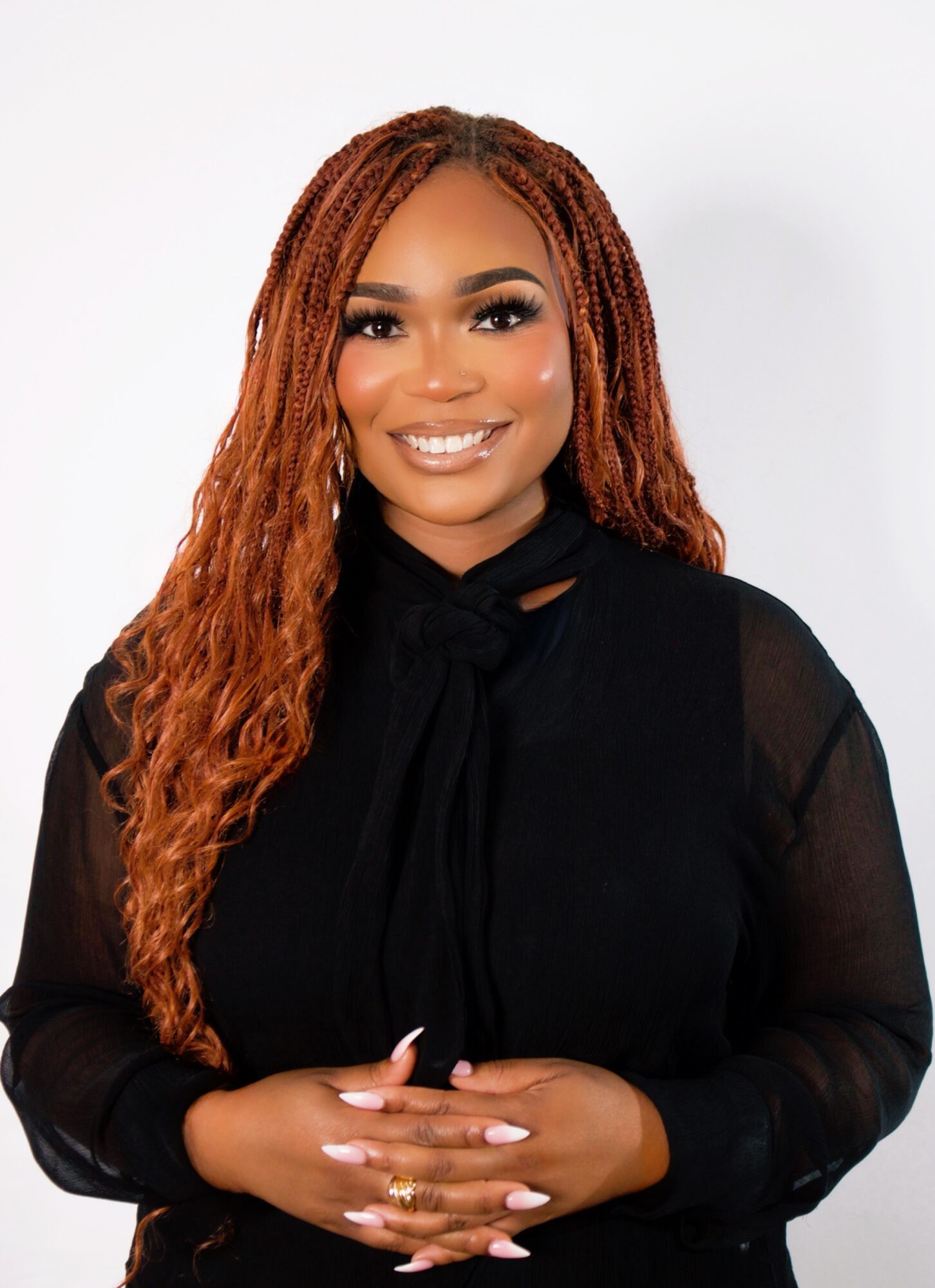 Portrait of a smiling woman with long, curly hair wearing a black top, hands clasped in front, against a white background.