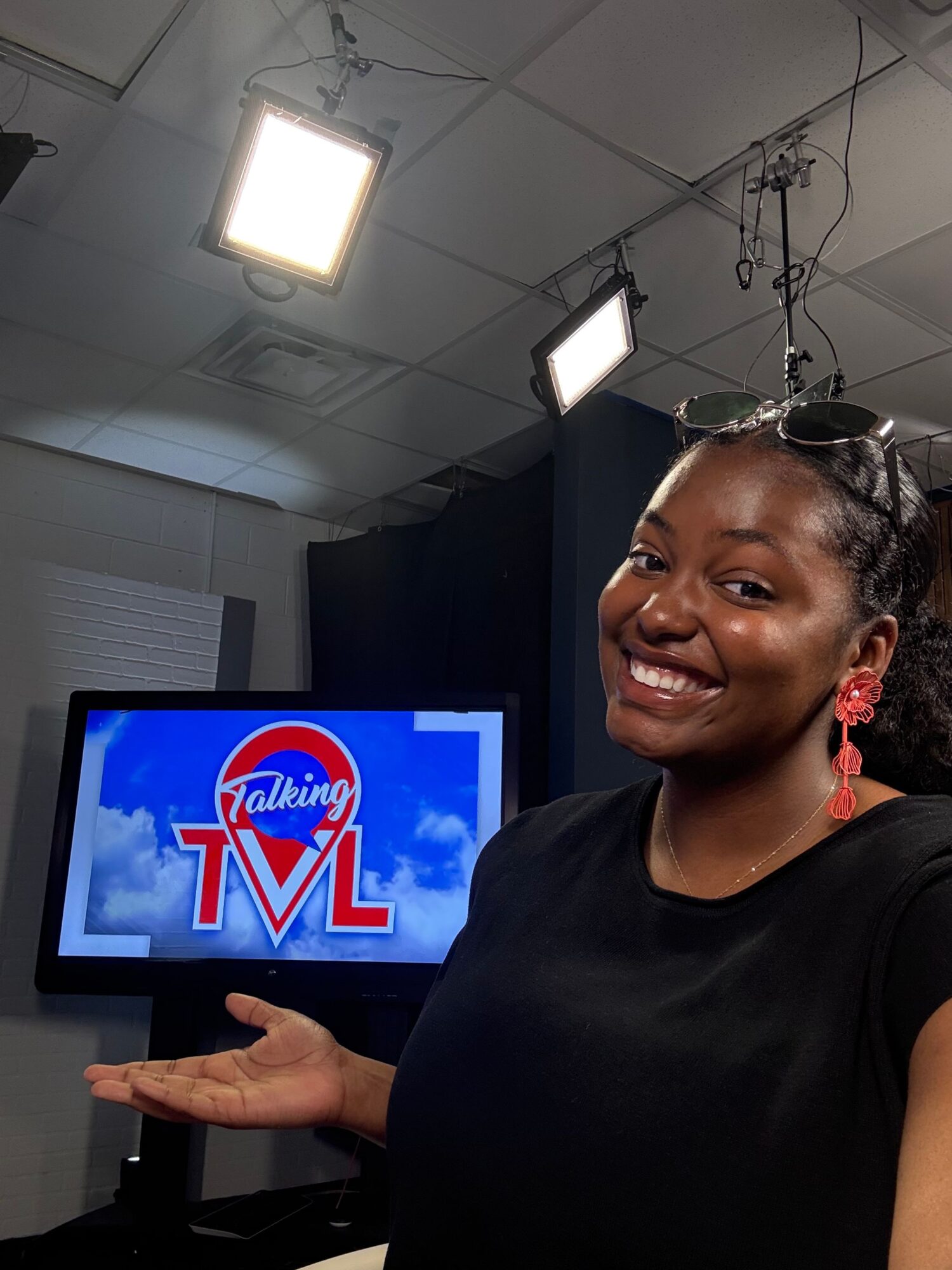 Woman smiling and pointing at a TV screen displaying a logo, in a studio setting.