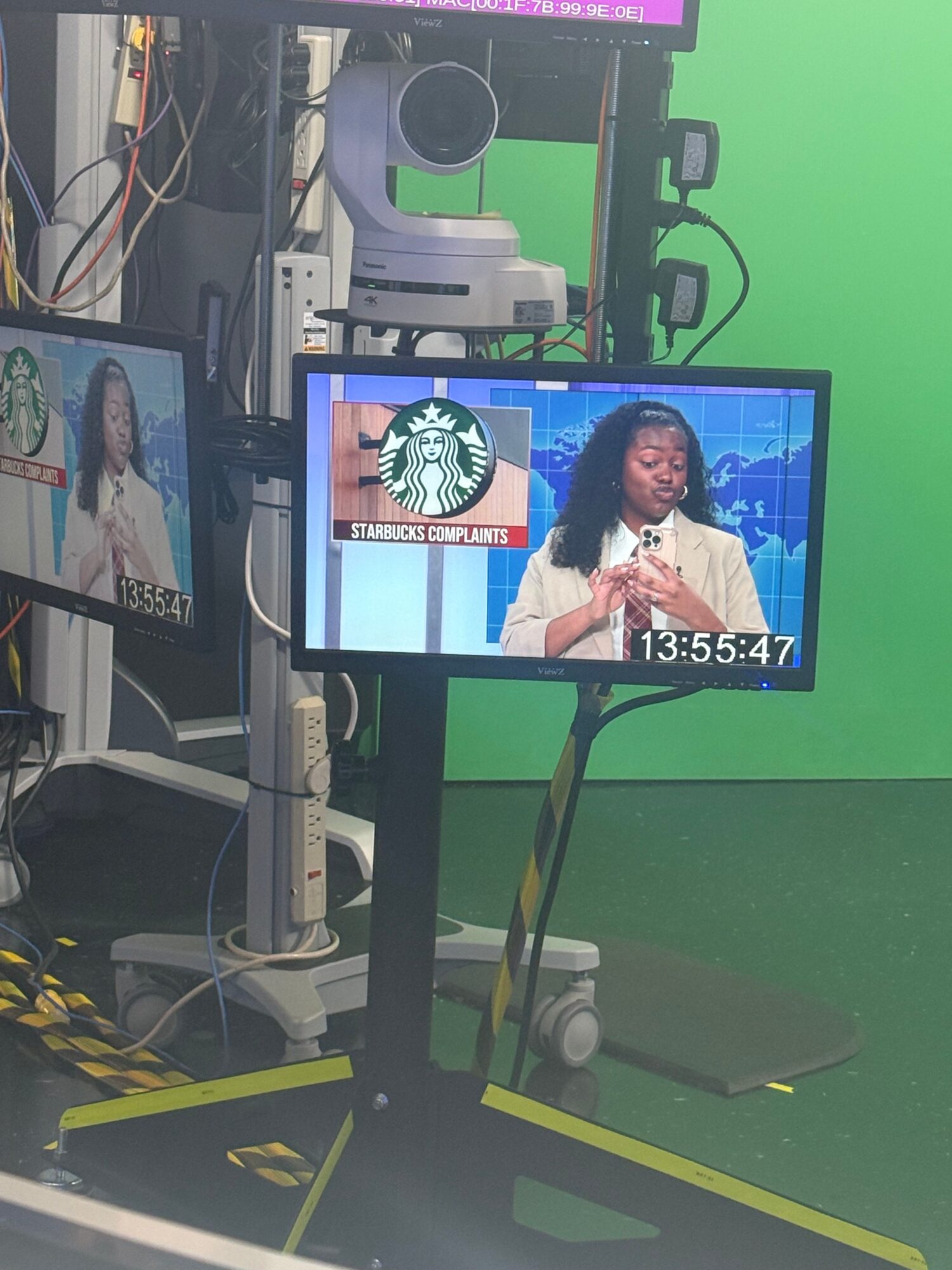 A computer monitor displays a news anchor and a Starbucks logo, with a green background and various equipment around.