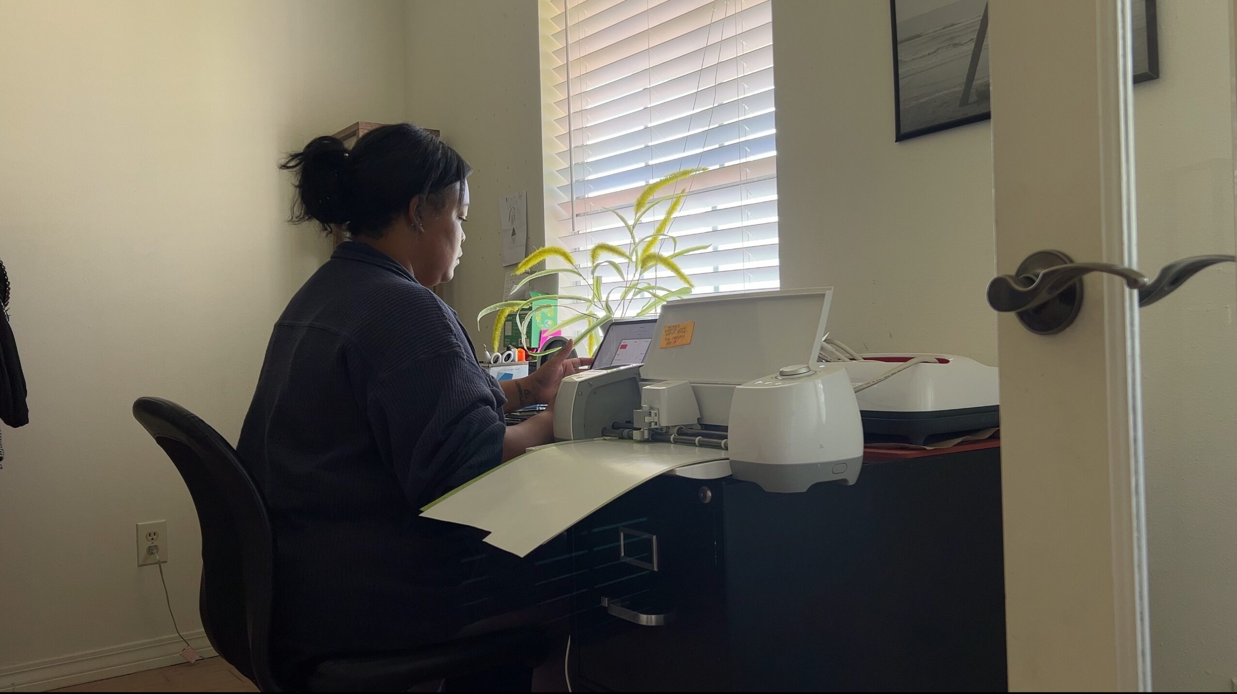 Person sitting at a desk using a laptop, with a window and blinds behind them.