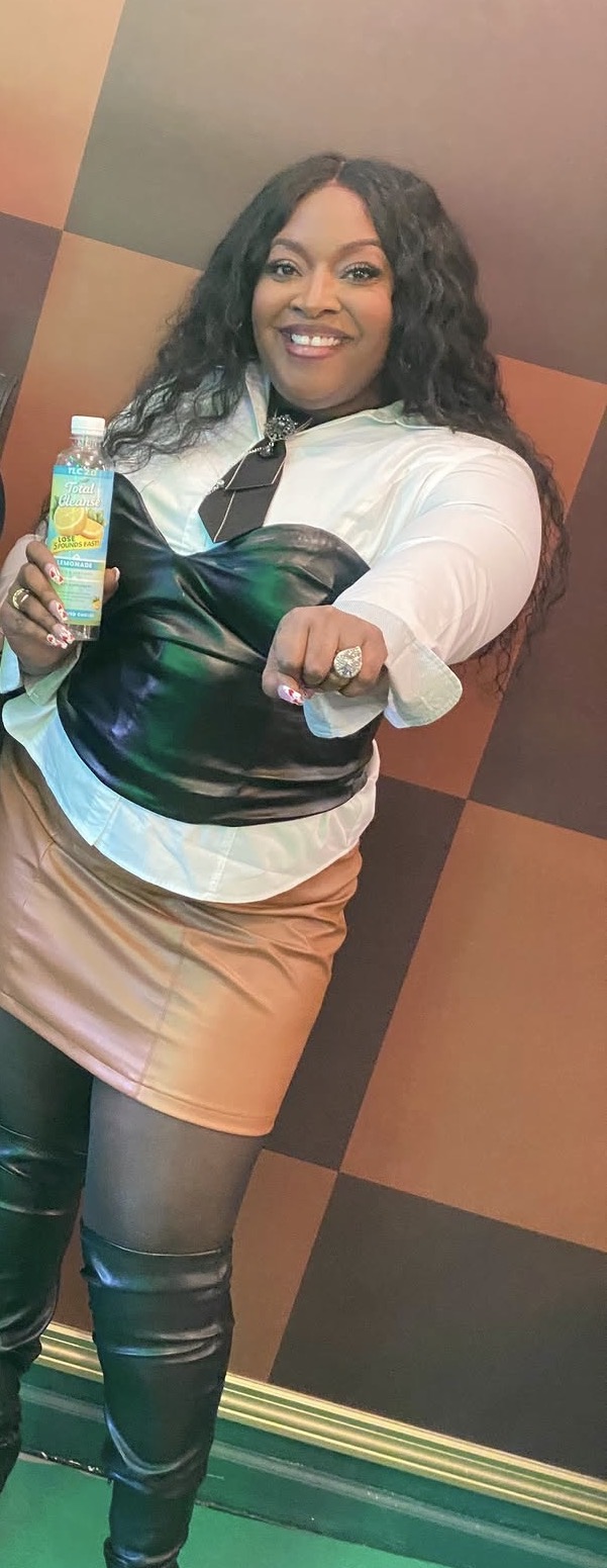 Woman smiling holding a colorful drink in a room with geometric wall patterns.