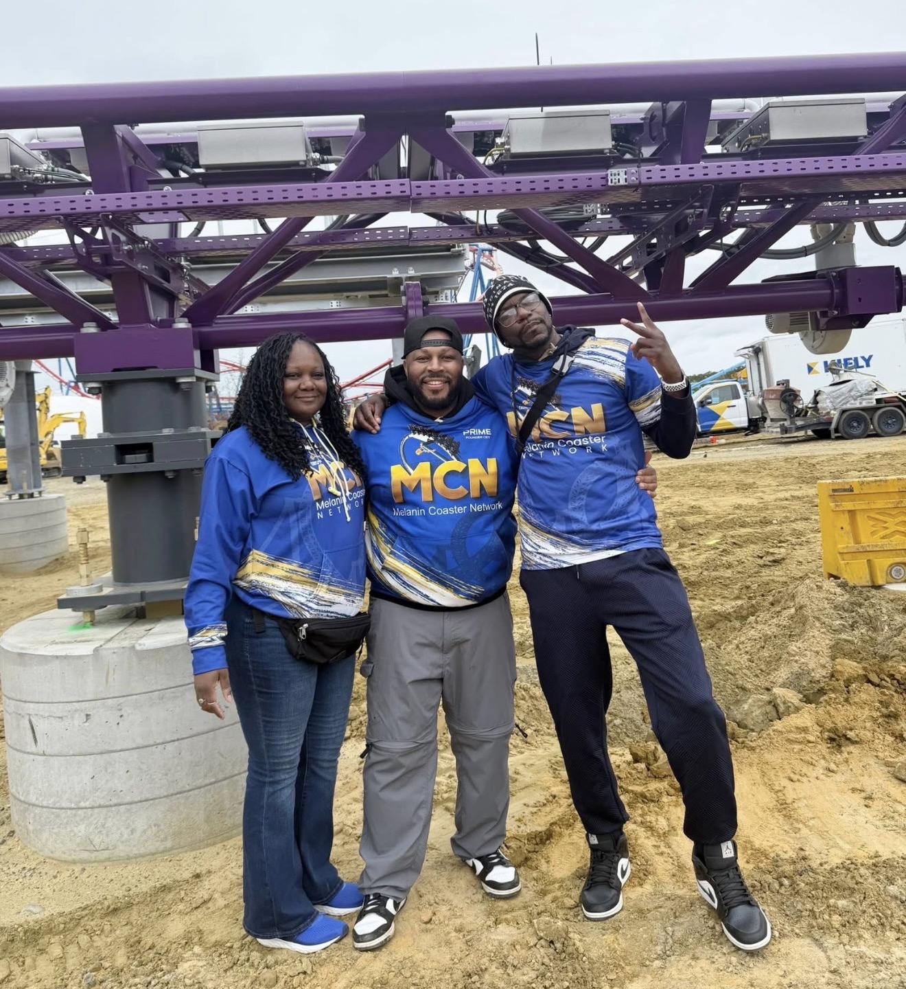 Three people stand in front of a purple amusement park ride, smiling and posing for the photo.