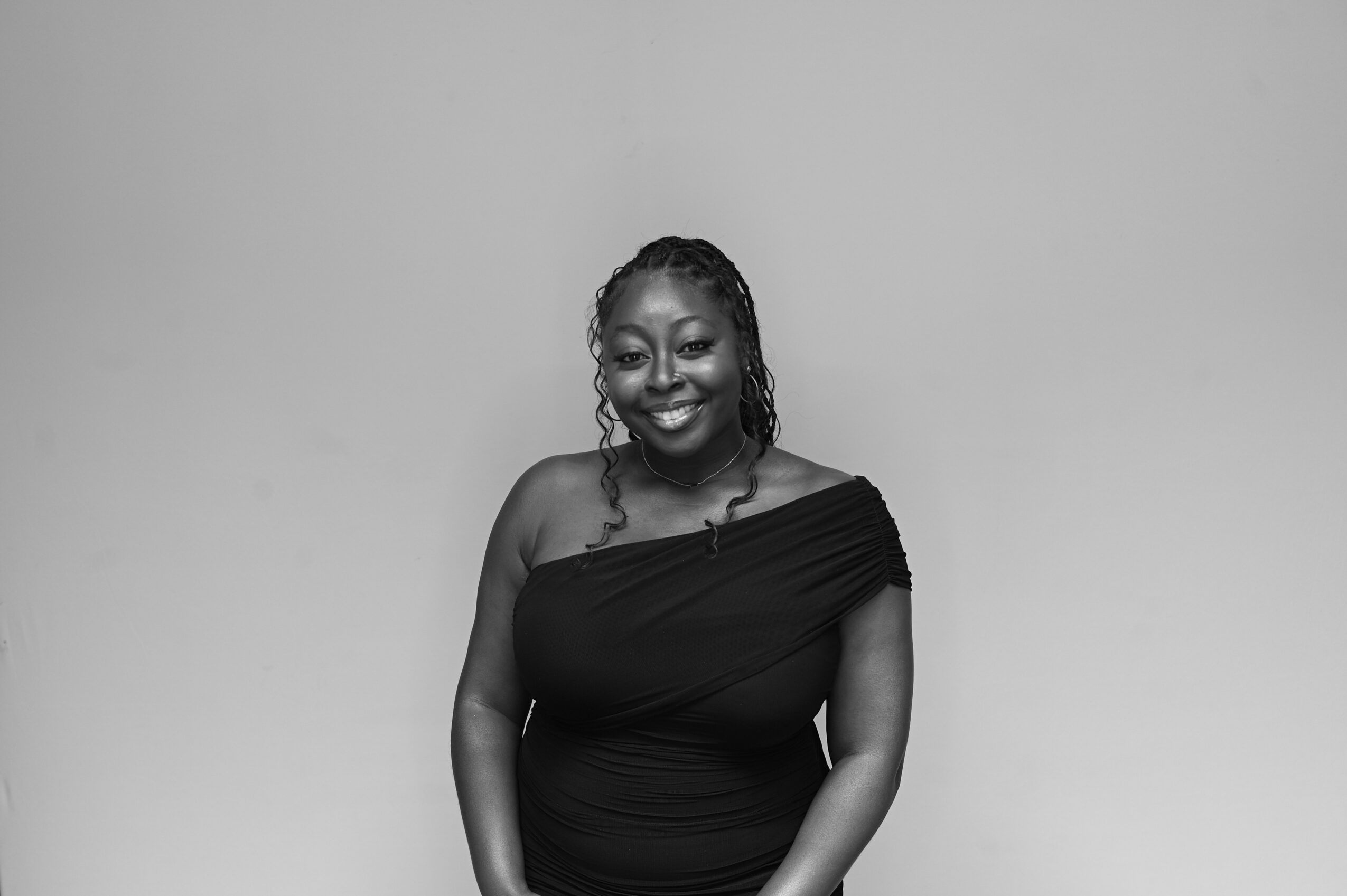 Woman smiling, wearing a one-shoulder dress, standing against a plain background.