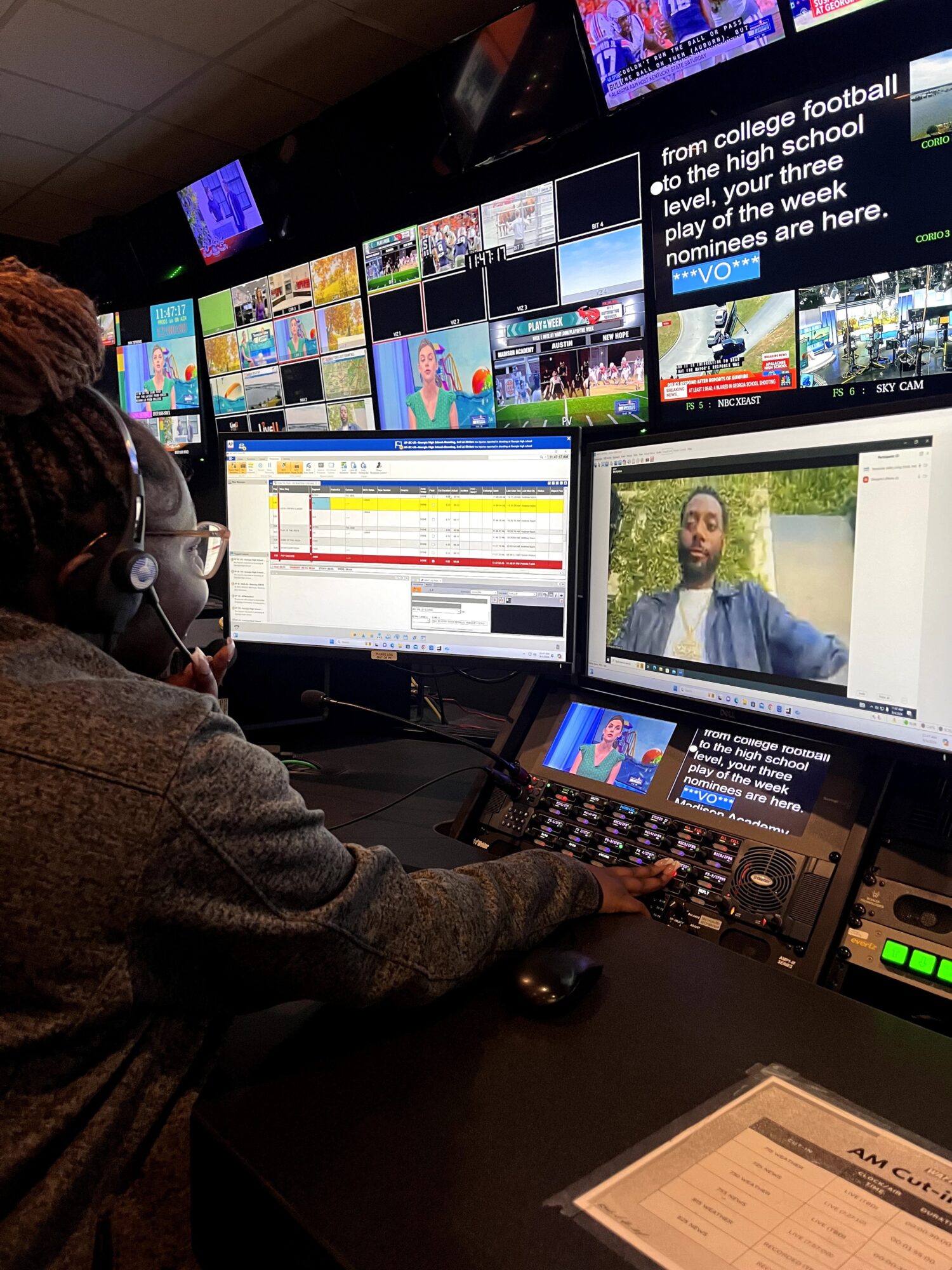 Person working at a control station with multiple monitors, including a video call and news screens.