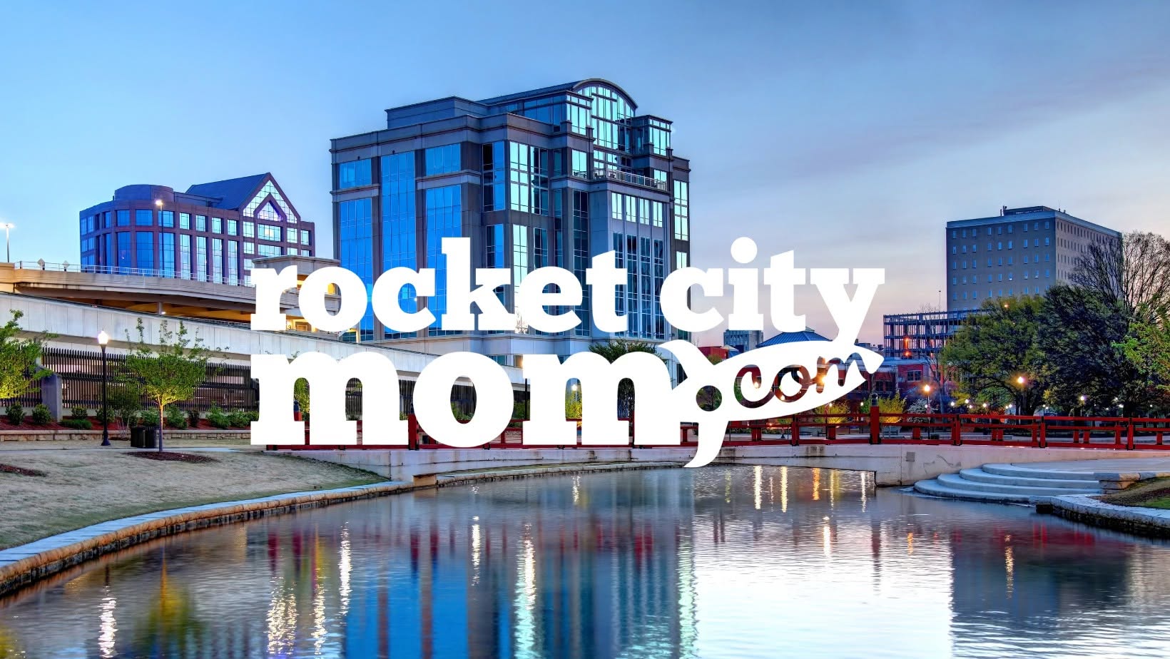 City skyline with modern buildings reflected in water, with text 'rocket city mom.com' overlayed.
