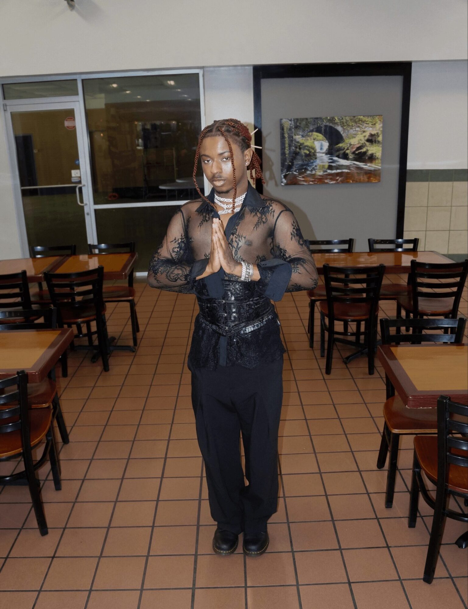 Woman with braided hair and black lace top standing with hands together in a restaurant setting.